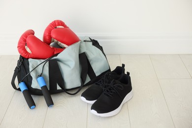 Photo of Stylish bag with sports equipment on floor indoors. Space for text