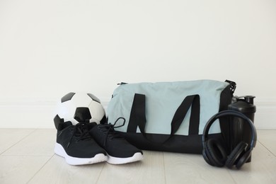 Photo of Stylish bag with sports equipment on floor indoors