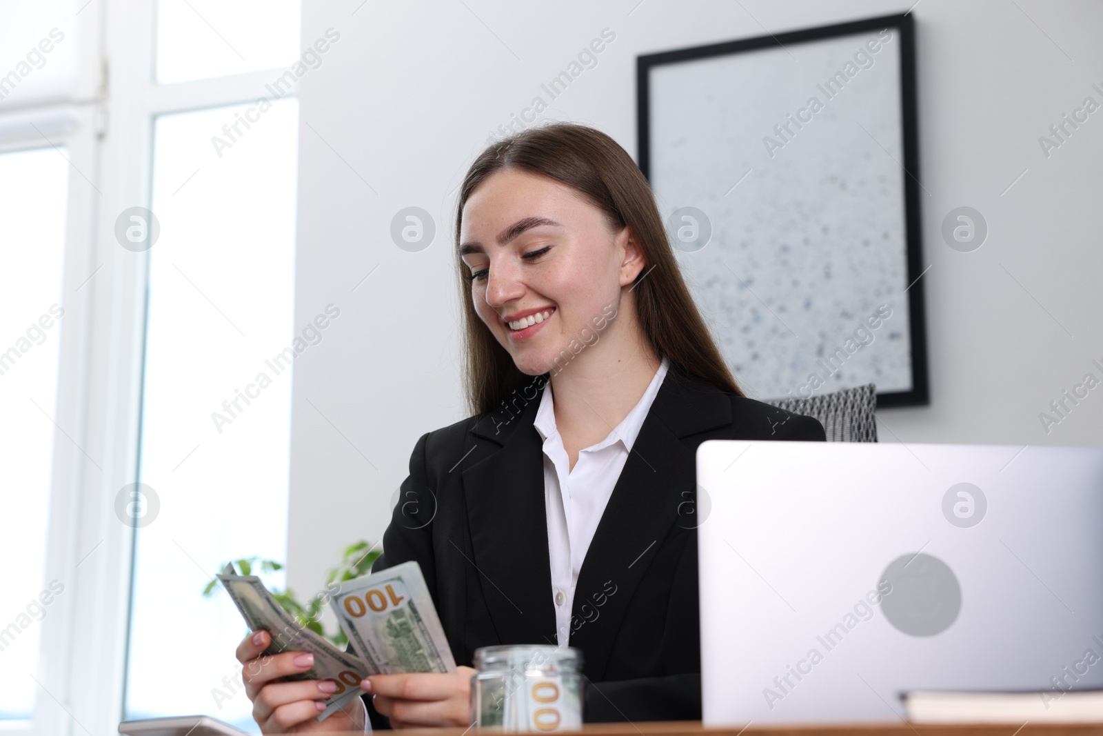 Photo of Woman counting dollar banknotes at table indoors