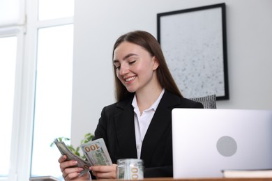 Photo of Woman counting dollar banknotes at table indoors