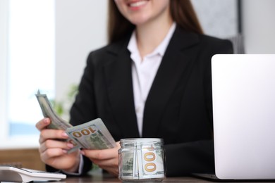 Photo of Woman counting dollar banknotes at table indoors, closeup