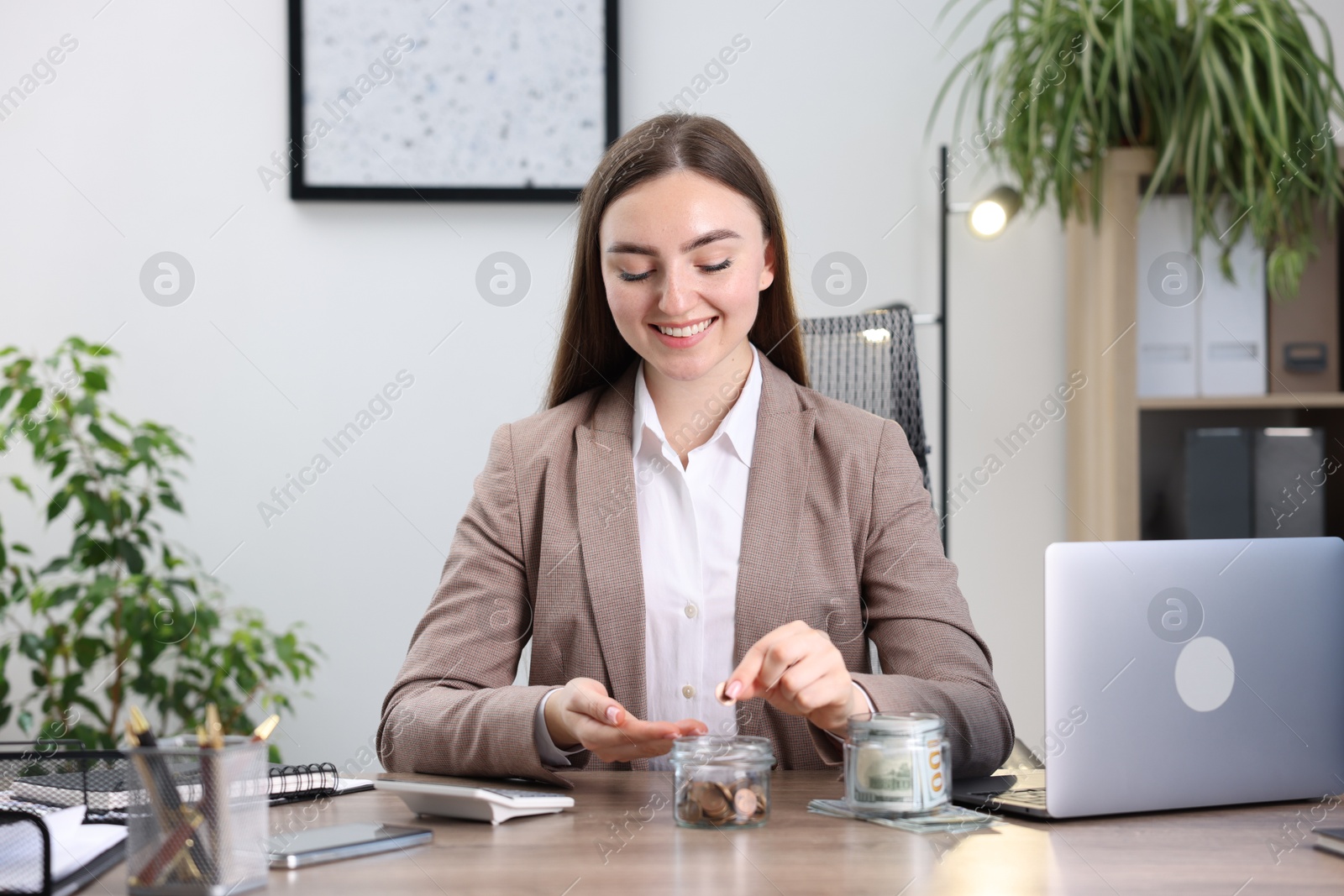 Photo of Woman putting coin into glass jar at wooden table indoors