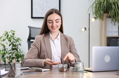 Photo of Woman putting coin into glass jar at wooden table indoors