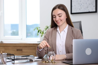 Photo of Woman putting coin into glass jar at wooden table indoors, space for text