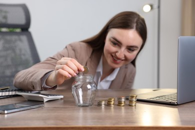 Photo of Woman putting coin into glass jar at wooden table indoors