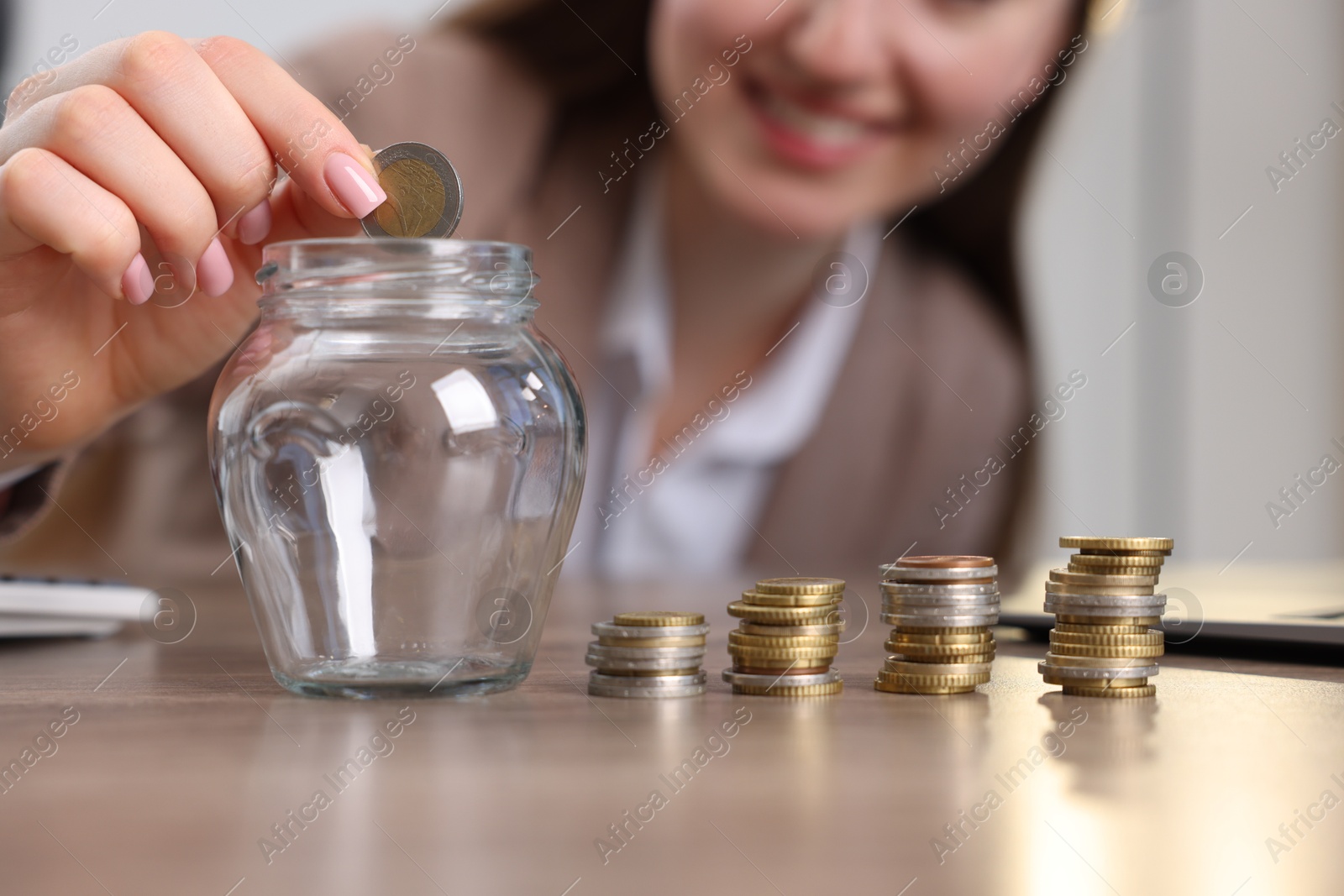 Photo of Woman putting coin into glass jar at table indoors, closeup
