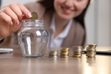Photo of Woman putting coin into glass jar at table indoors, closeup