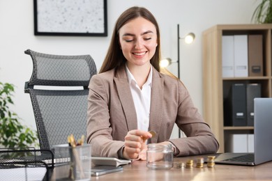Photo of Woman putting coin into glass jar at wooden table indoors