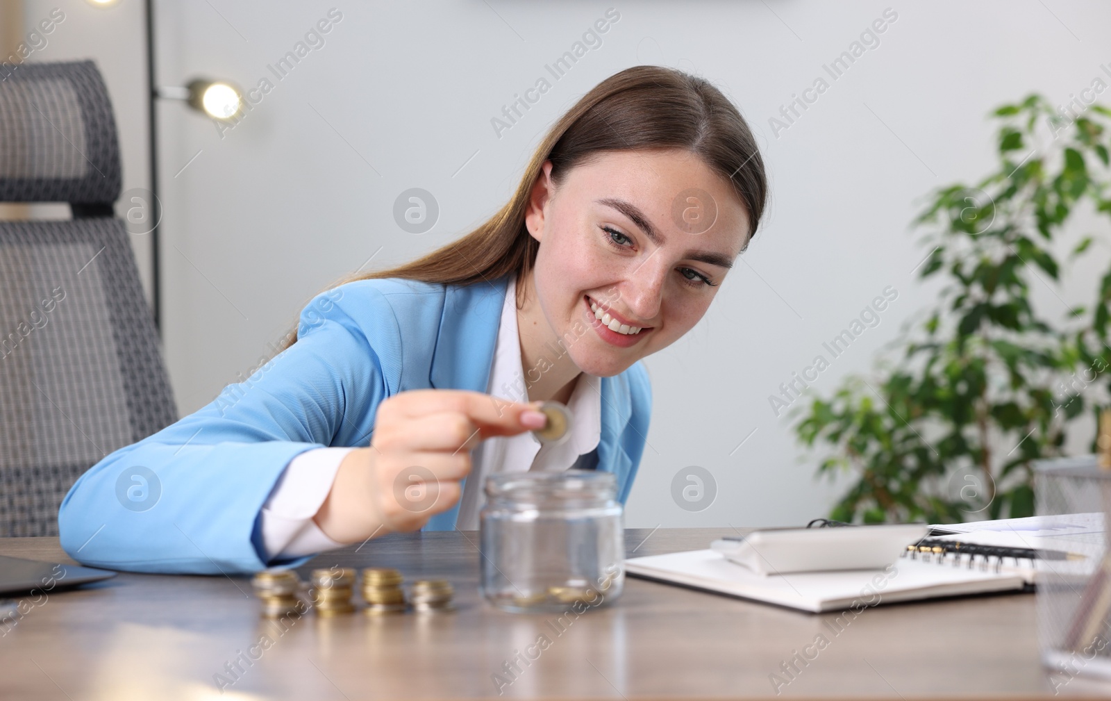 Photo of Woman putting coin into glass jar at wooden table indoors