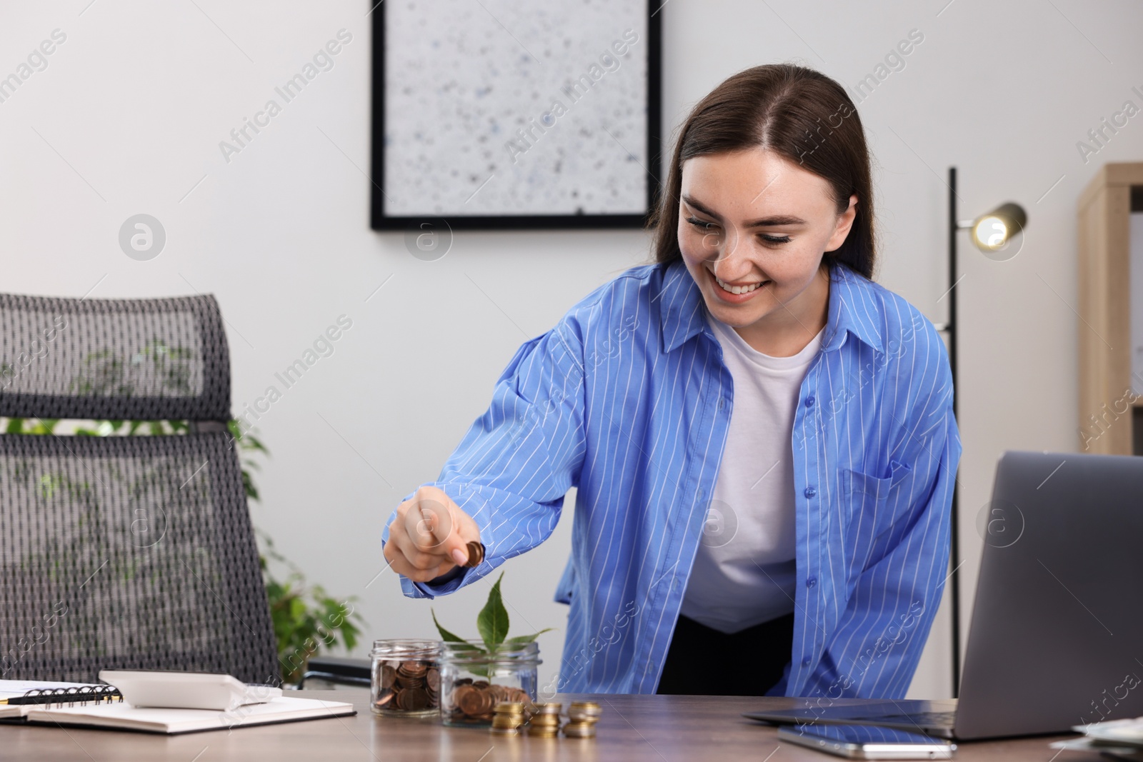 Photo of Woman putting coins into glass jar at wooden table indoors