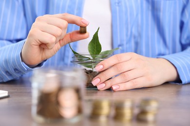 Photo of Woman putting coins into glass jar at wooden table indoors, closeup