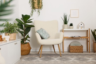 Photo of Stylish armchair with cushion, houseplants and decor in room. Interior design
