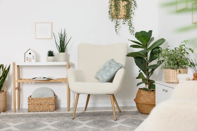 Photo of Stylish armchair with cushion, houseplants and decor in room. Interior design