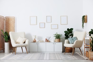 Photo of Stylish armchairs with cushions, cabinet, houseplants and decor in room. Interior design