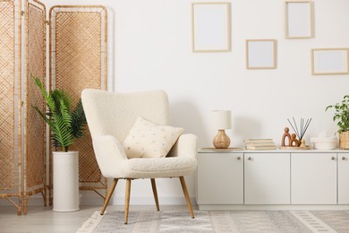 Photo of Stylish armchair with cushion, cabinet, houseplants and decor in room. Interior design