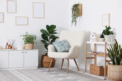 Photo of Stylish armchair with cushion, cabinet, houseplants and decor in room. Interior design