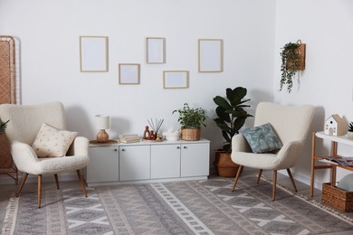Photo of Stylish armchairs with cushions, cabinet, houseplants and decor in room. Interior design