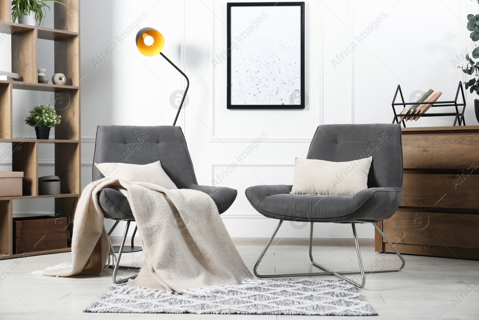 Photo of Stylish armchairs with pillows, blanket, dresser and shelving unit indoors. Interior design