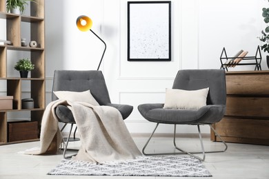 Photo of Stylish armchairs with pillows, blanket, dresser and shelving unit indoors. Interior design
