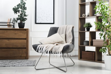 Photo of Stylish armchair with pillow, blanket, dresser and shelving unit indoors. Interior design