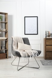 Photo of Stylish armchair with pillow, blanket, dresser and shelving unit indoors. Interior design