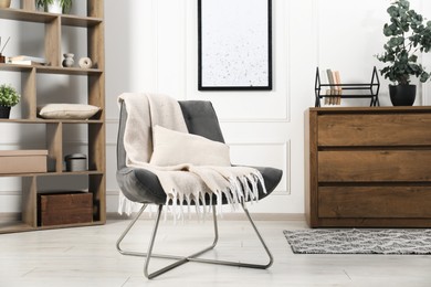 Photo of Stylish armchair with pillow, blanket, dresser and shelving unit indoors. Interior design