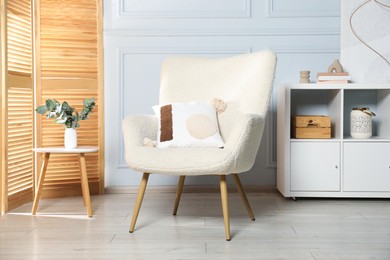 Photo of Stylish armchair with pillow, cabinet and decor indoors. Interior design
