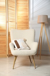 Photo of Stylish armchair with pillow, lamp and folding screen indoors. Interior design