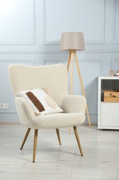 Photo of Stylish armchair with pillow and lamp indoors. Interior design