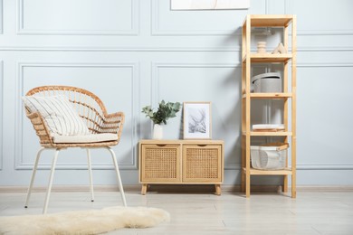 Photo of Stylish armchair with pillow, cabinet and decor indoors. Interior design