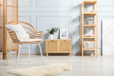 Photo of Stylish armchair with pillow, cabinet and decor indoors. Interior design