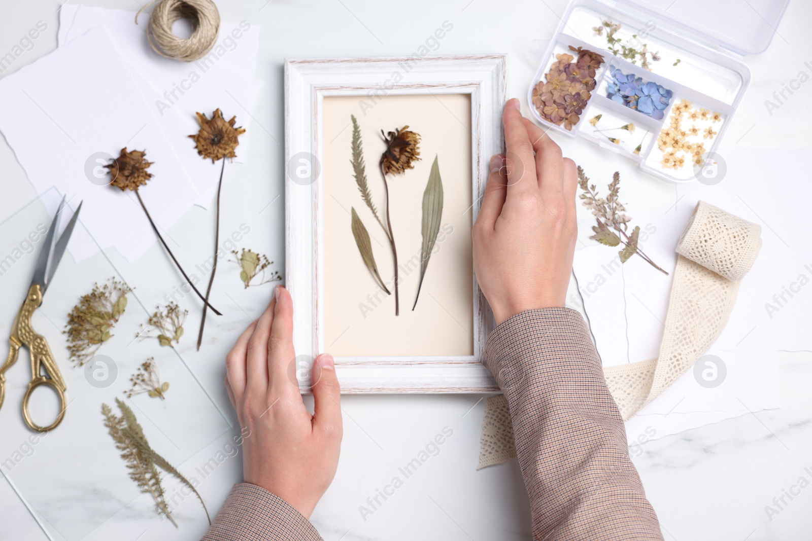 Woman with dry flowers and picture frame at white marble table, top view Photo of Woman with dry flowers and picture frame at white marble table, top view