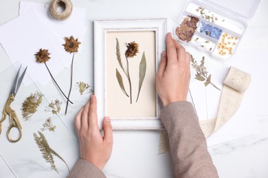 Photo of Woman with dry flowers and picture frame at white marble table, top view