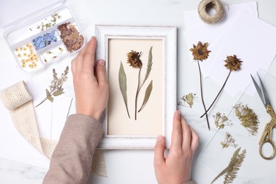 Photo of Woman with dry flowers and picture frame at white marble table, top view