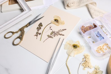 Photo of Dry flowers, tweezers, scissors and paper on white marble table, closeup