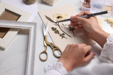 Photo of Woman putting dry flowers into paper sheet at white marble table, closeup