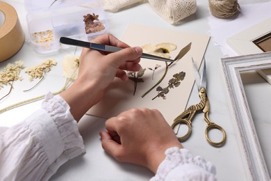 Photo of Woman putting dry flowers into paper sheet at white marble table, closeup