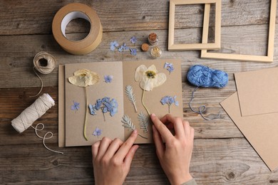 Photo of Woman putting dry flowers into notebook at wooden table, top view