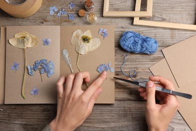 Photo of Woman putting dry flowers into notebook at wooden table, top view
