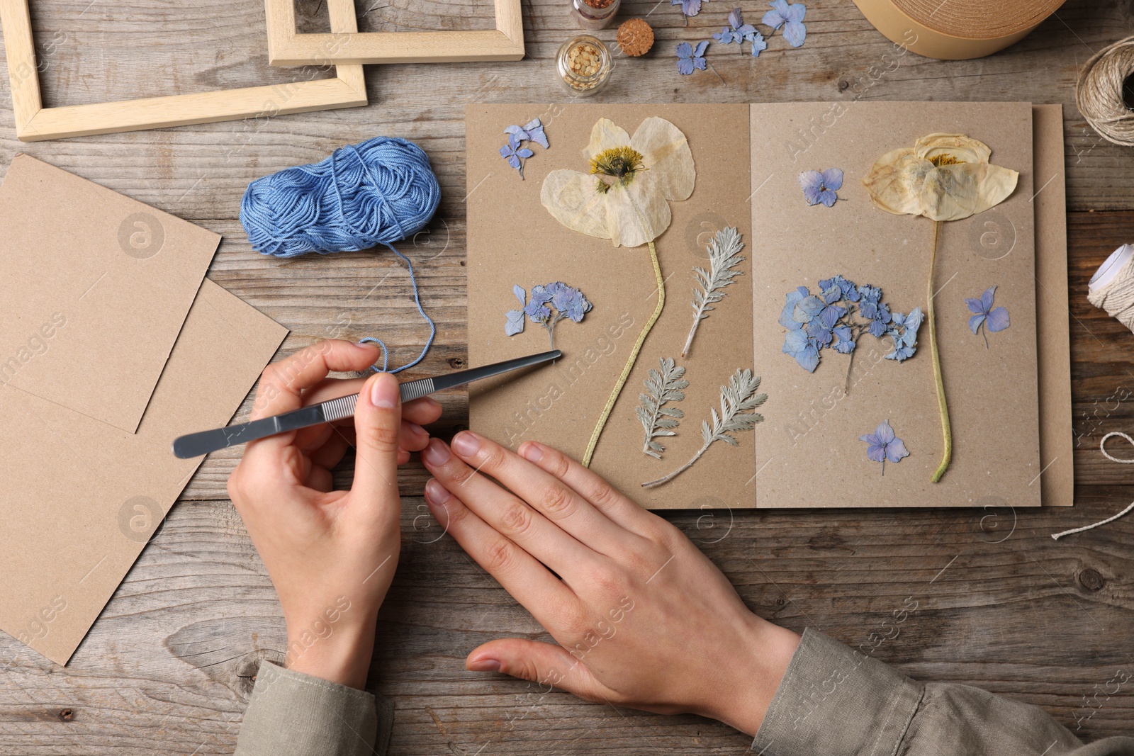 Photo of Woman putting dry flowers into notebook at wooden table, top view