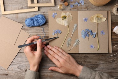 Photo of Woman putting dry flowers into notebook at wooden table, top view