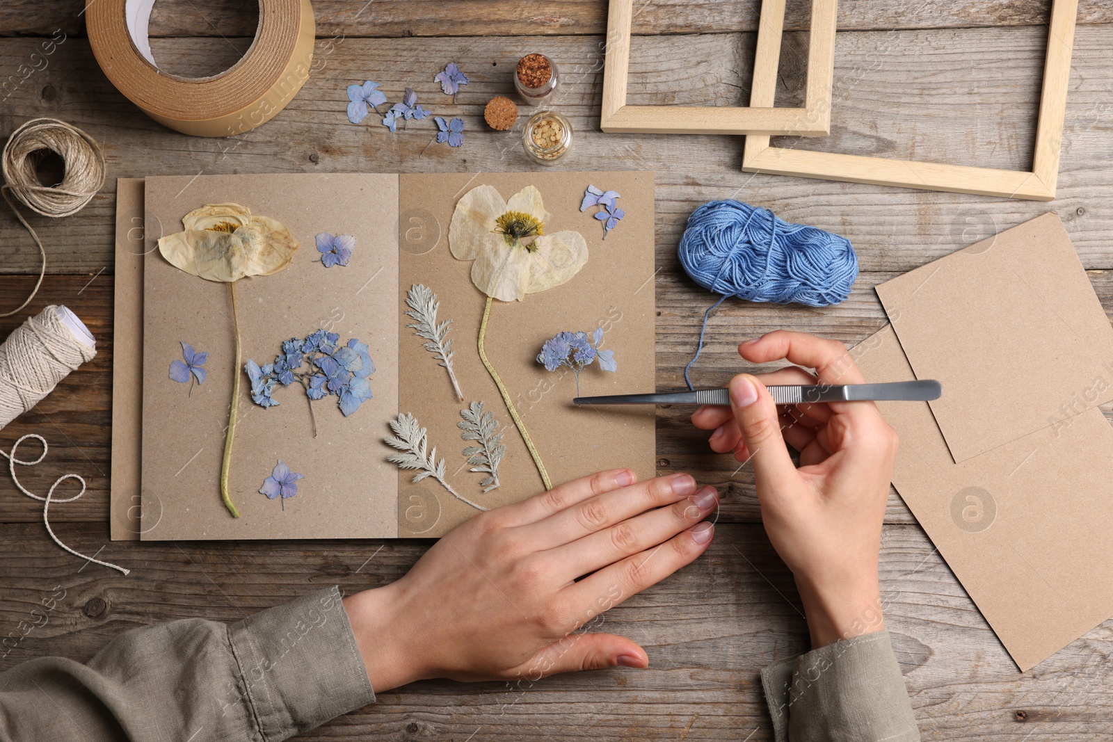 Woman putting dry flowers into notebook at wooden table, top view Photo of Woman putting dry flowers into notebook at wooden table, top view
