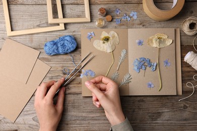 Photo of Woman putting dry flowers into notebook at wooden table, top view