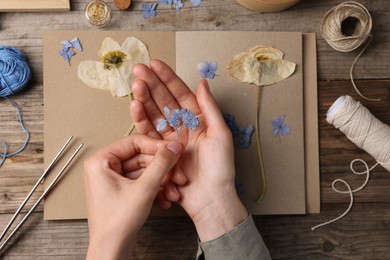 Photo of Woman putting dry flowers into notebook at wooden table, top view