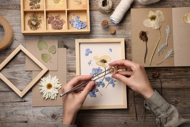 Photo of Woman putting dry flowers into picture frame at wooden table, top view