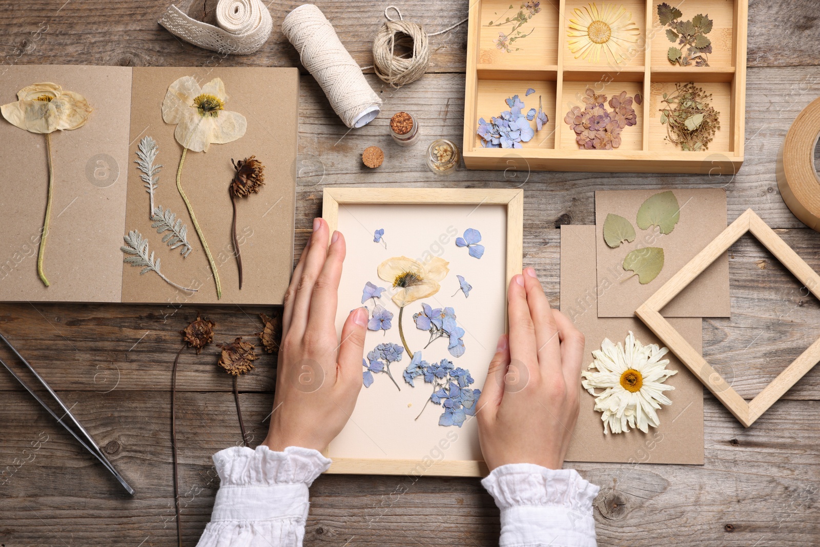 Woman putting dry flowers into picture frame at wooden table, top view Photo of Woman putting dry flowers into picture frame at wooden table, top view