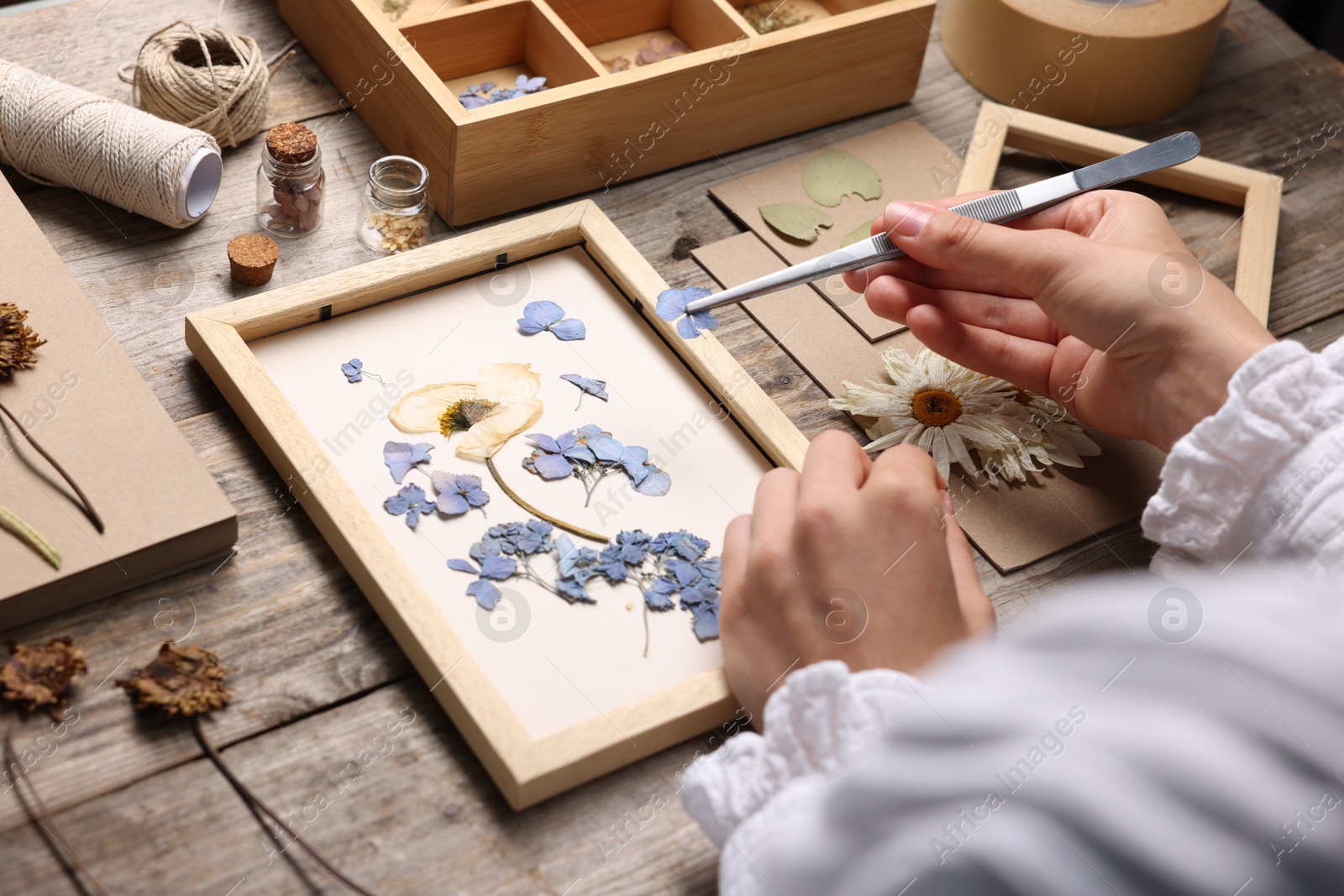 Woman putting dry flowers into picture frame at wooden table, closeup Photo of Woman putting dry flowers into picture frame at wooden table, closeup