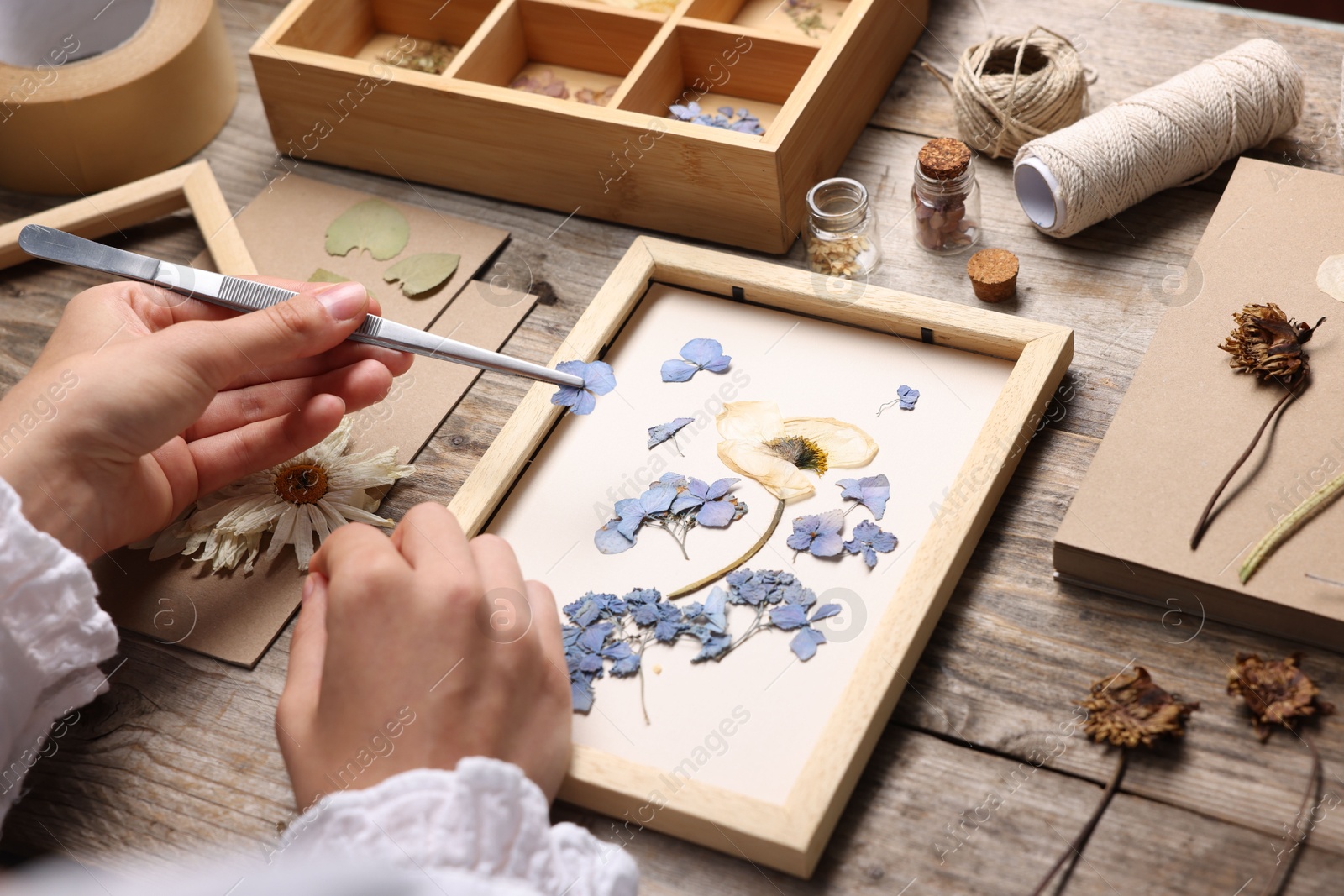 Woman putting dry flowers into picture frame at wooden table, closeup Photo of Woman putting dry flowers into picture frame at wooden table, closeup