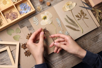 Photo of Woman putting dry flowers into notebook at wooden table, top view