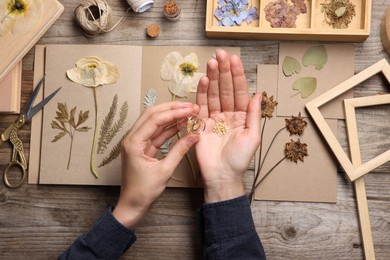 Photo of Woman putting dry flowers into notebook at wooden table, top view
